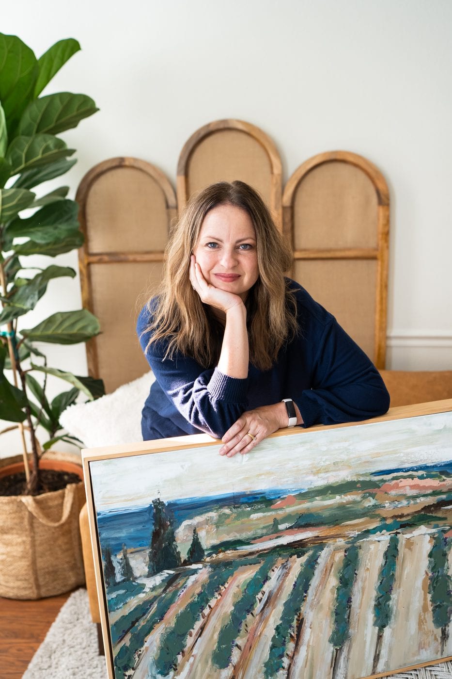 Jen Bell, painter and instructor, in her Fresno County studio with a large landscape painting of California vineyards.